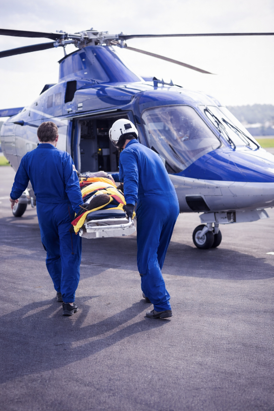 A medical helicopter crew carries a stretcher with a patient into the helicopter.