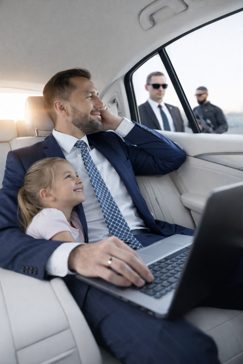 A man in a suit hugs a child in a luxury car